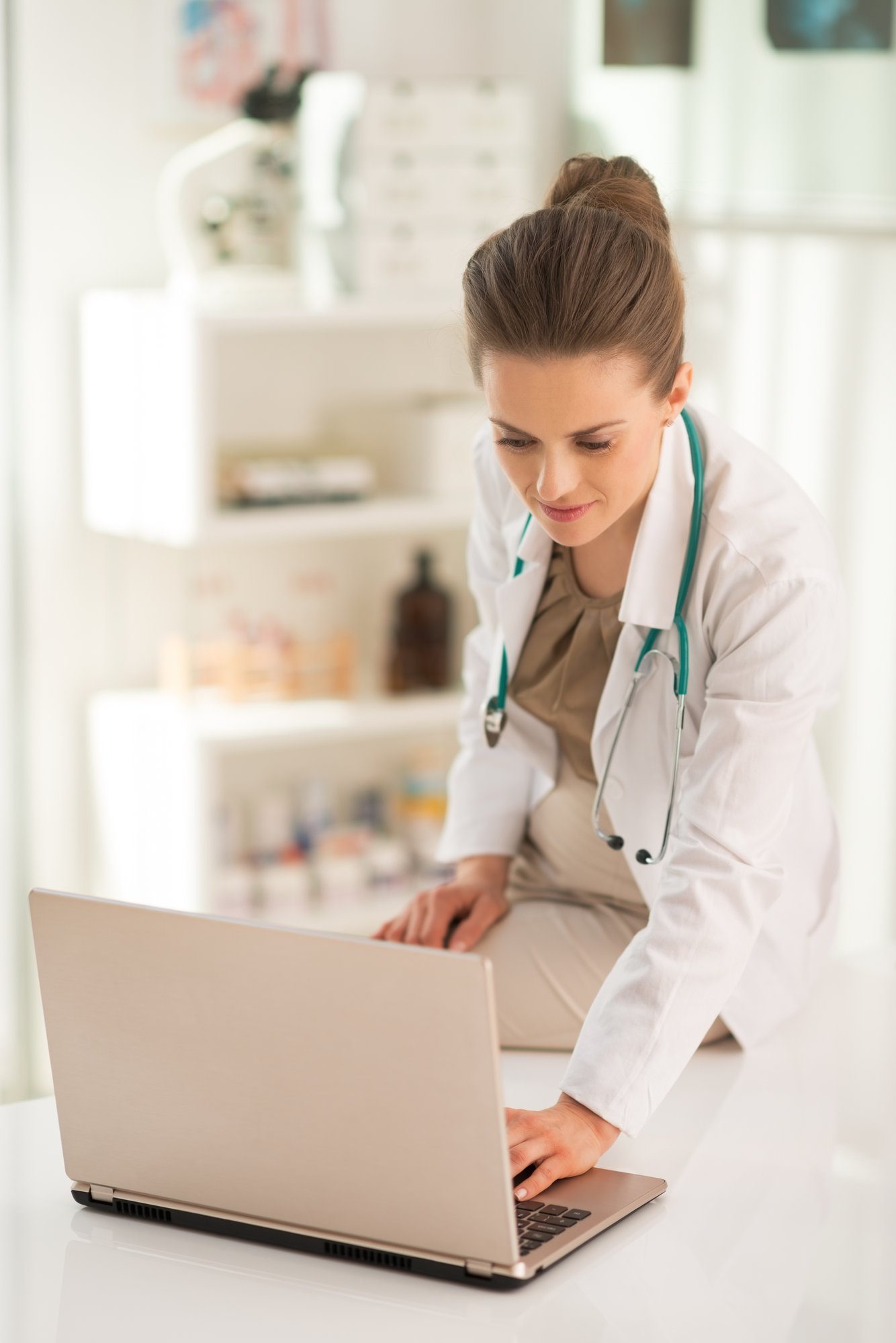 woman doctor with stethoscope looking at laptop in office