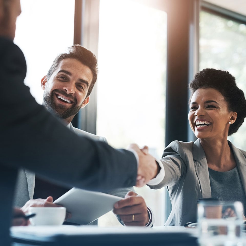 Business professionals in a meeting room, shaking hands over a successful agreement. The image represents managed IT services for financial firms and emphasizes IT support for financial services
